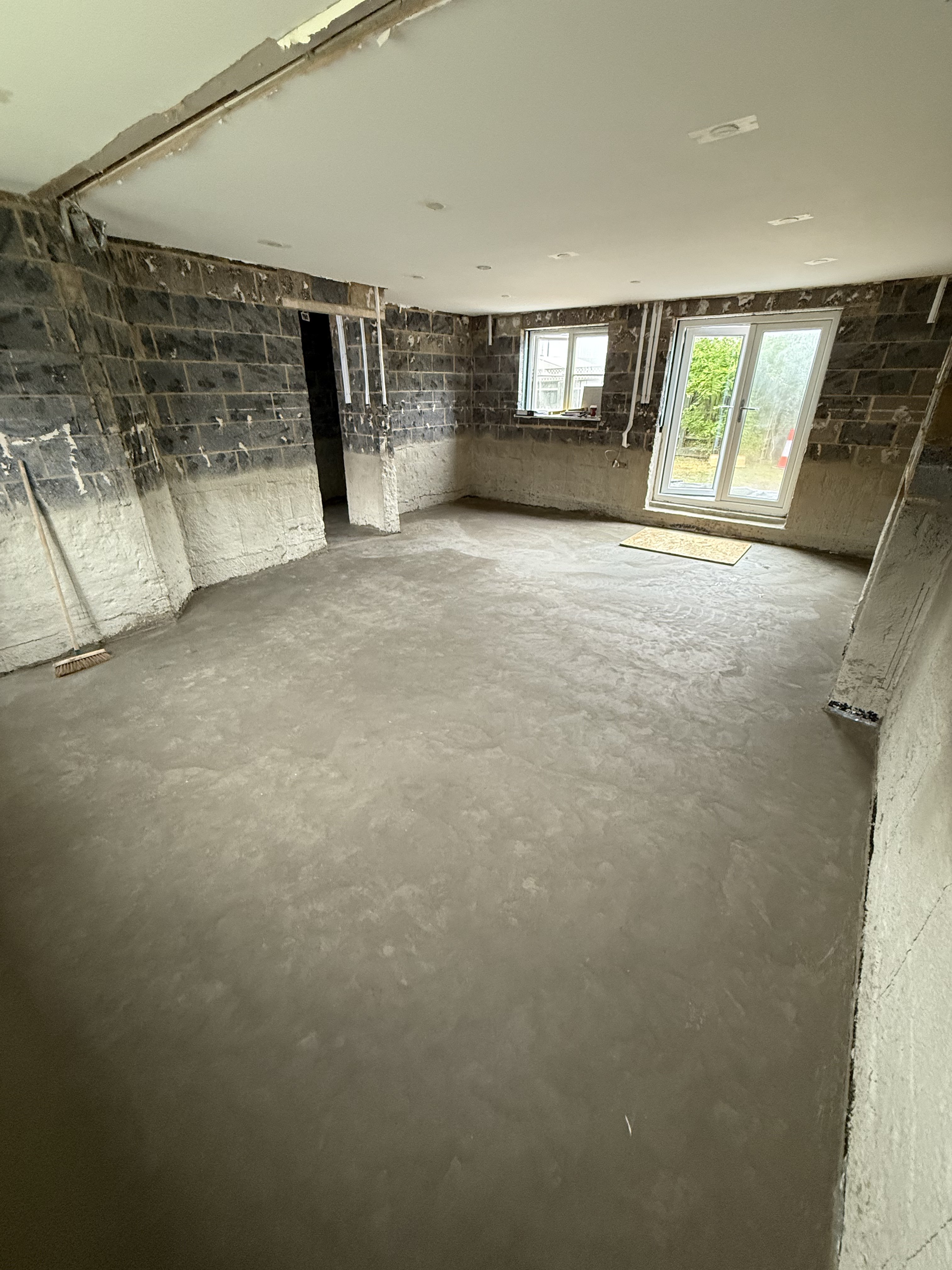 Living room at early stage — cement tanking sprayed onto walls, concrete slab waiting for its resin coat before Foamglas insulation and sump pump channelling