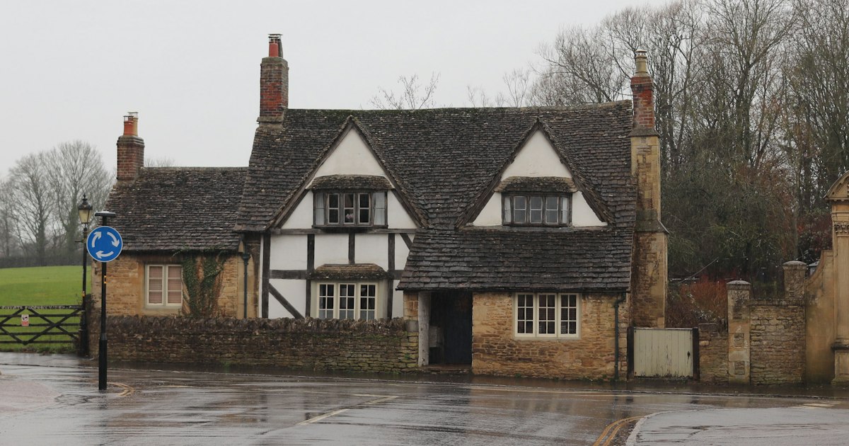 A half-timbered English village house beside a wet road junction on an overcast day